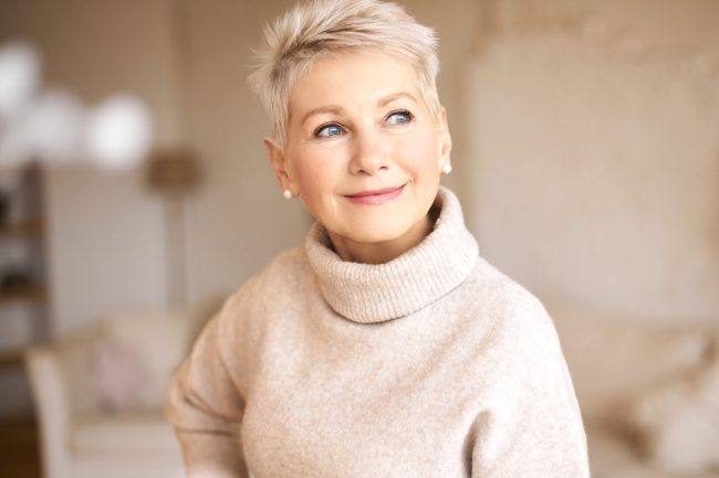 People, age and maturity. Close up shot of elegant blonde middle aged woman with short haircut looking up with pensive smile, thinking about something pleasant, making plans, recollecting old days healthy aging